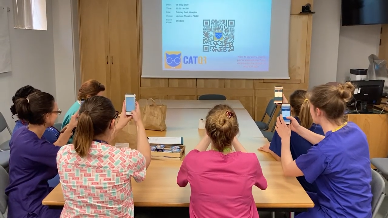 Junior doctors in a classroom using the CATQR mobile app to scan a QR code projected on the whiteboard.